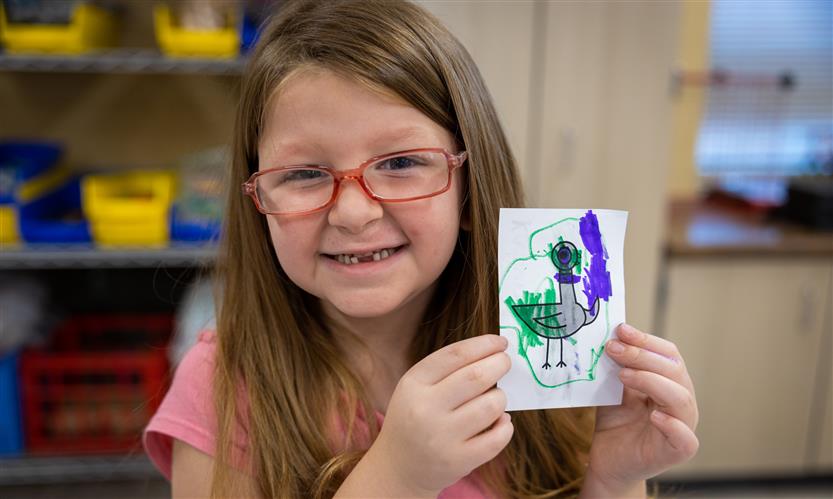 A girl smiles while holding up a drawing